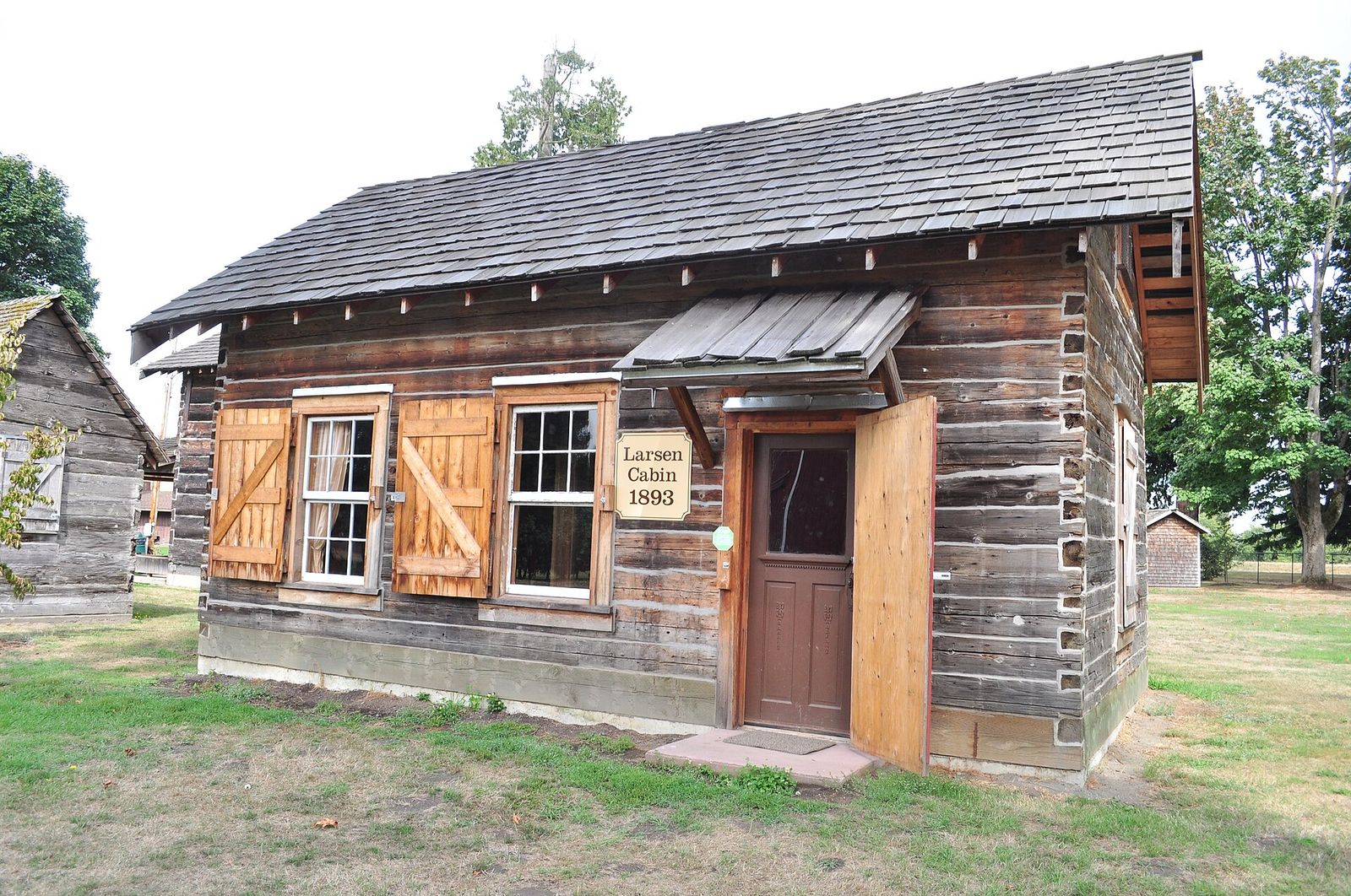 The Larsen Cabin, a weathered 1893 log cabin with wooden shutters and a small door overhang, in Pioneer Park, Ferndale